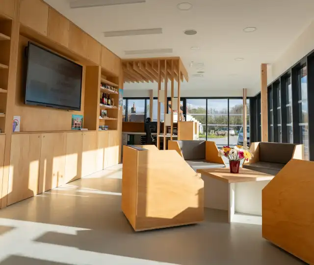Intérieur moderne d'un centre d'accueil au port fluvial d'Aire-sur-la-Lys avec boiseries naturelles, mobilier contemporain et grandes baies vitrées